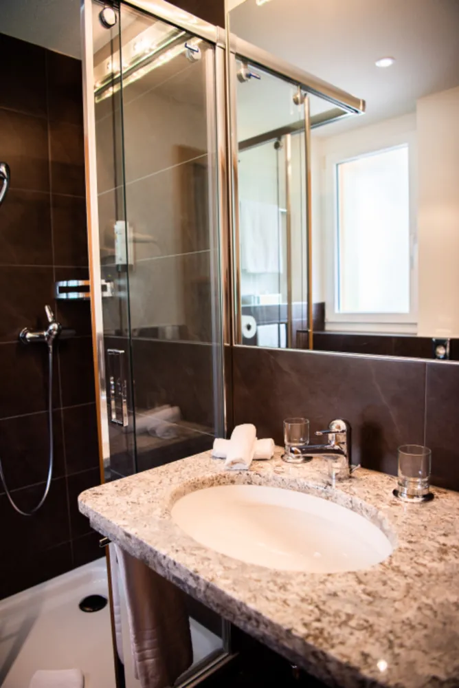 Bathroom with brown tile walls, glass shower and a stone vanity top